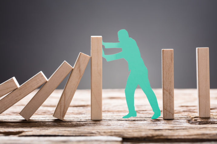 Green Paper Man Stopping Wooden Domino Blocks