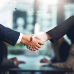 Two men in suits shake hands - only their arms are visible