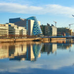 Modern buildings and offices on Liffey river in Dublin on a bright sunny day. Bridge on the right is a famous Harp bridge.