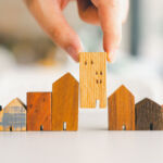 Hand choosing mini wood house model from model and row of coin money on wood table, selective focus, Planning to buy property. Choose what's the best. A symbol for construction ,ecology, loan concepts